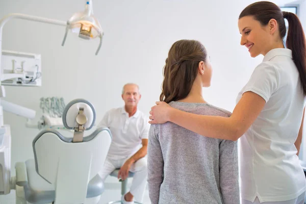 Vrouwelijke assistent praten met meisje patiënt in het bijzijn van tandarts op — Stockfoto