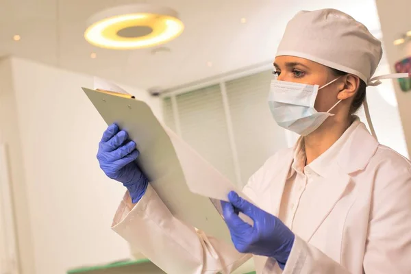 Doctor wearing face mask and cap while examining medical result — Stock Photo, Image