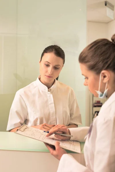 Doctor signing on clipboard while receptionist standing at clini — Stock Photo, Image