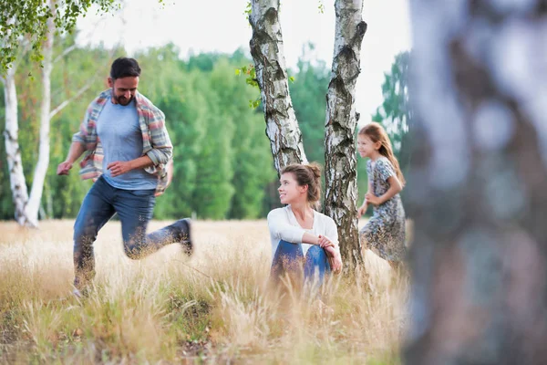 農地のフィールドで娘と遊んでいる男を見ている女性 — ストック写真