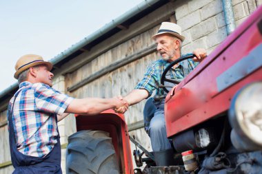 Çiftçiler çiftlikte traktörün yanında el sıkışıyor.