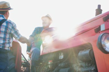 Çiftçiler çiftlikte traktörün yanında el sıkışıyor.