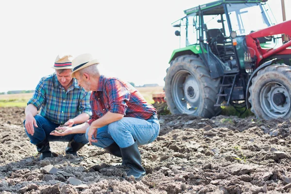 Coworkers examining soil on field at farm against sky