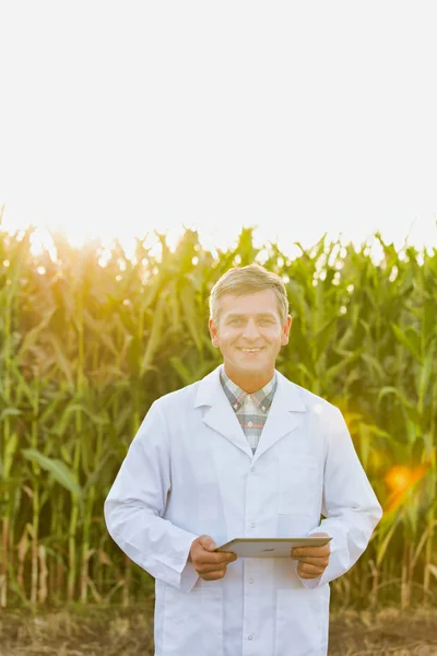 Mature scientist with digital tablet inspecting crops at farm