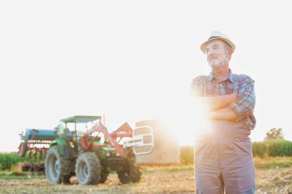 自信的高级农夫的画像站立反对拖拉机在农场 — 图库照片