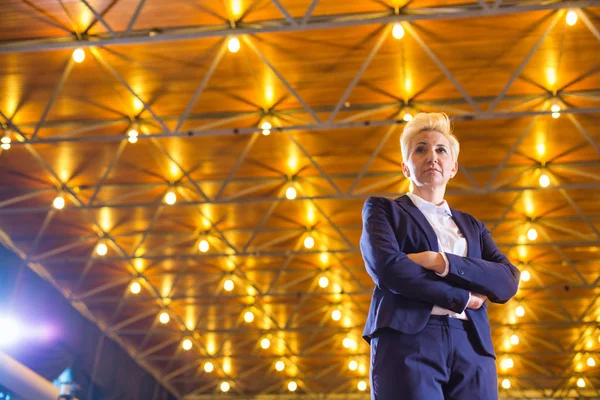 Confident blond businesswoman standing with arms crossed against — Stock Photo, Image