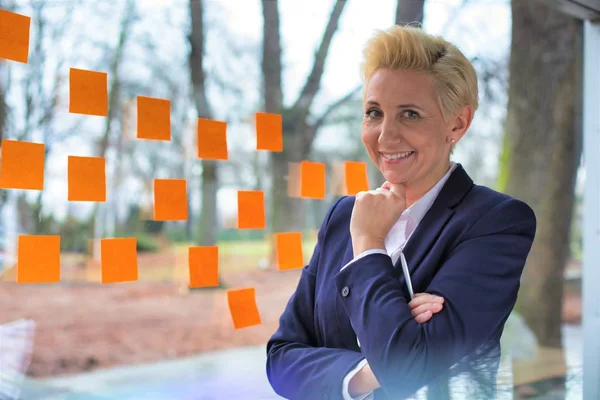 Une femme d'affaires mature souriante debout contre les fenêtres du bureau — Photo