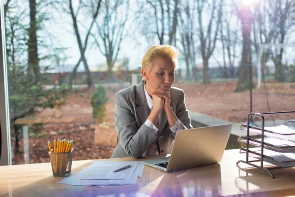 Confident mature businesswoman sitting with laptop at desk again — Φωτογραφία Αρχείου