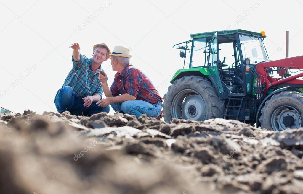 Coworkers examining soil on field at farm against sky