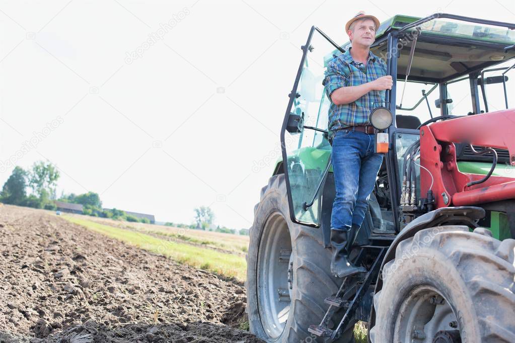 farmer standing on harvester at field against sky