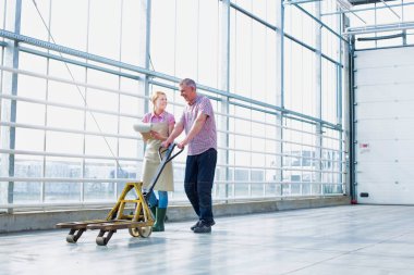 Farmer pulling pallet jack while discussing with colleague at greenhouse