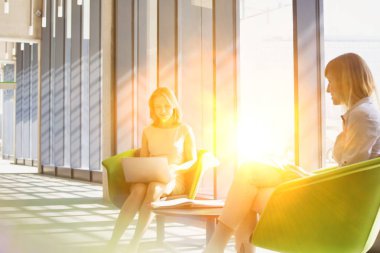 İki kadın ofiste çalışıyor ve kahve içiyor.