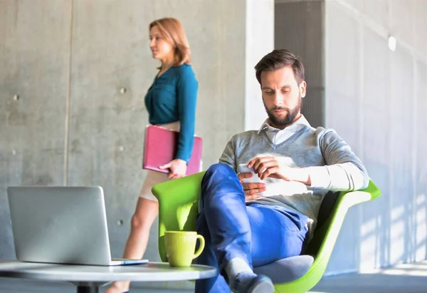 オフィスの待合室で緑の椅子に座っている間 スマートフォンを使用してひげそりのビジネスマン — ストック写真