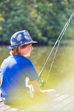 Young boy fishing in lake while sitting on pier