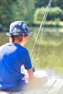 Young boy fishing in lake while sitting on pier