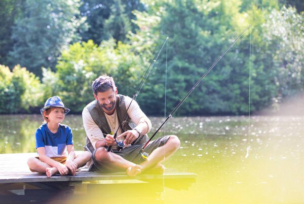 Отец и сын рыбачат в озере, сидя на пирсе
