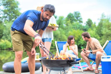 İskelede arkadaşlarıile barbekü ızgara yemek hazırlamak için körük kullanan adam