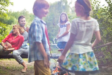 Aileler parktaki bankta otururken kamp alanında duran çocuklar