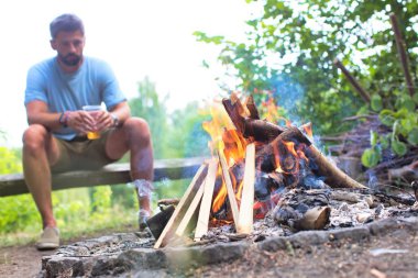 Man drinking beer while sitting on bench at park with bonfire