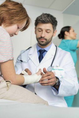 Klinikte çocuğun eline bandaj bağlayan çocuk doktoru.