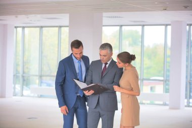 Gülümseyen olgun iş adamı yeni ofisindeki meslektaşlarına el kol hareketi yapıyor.