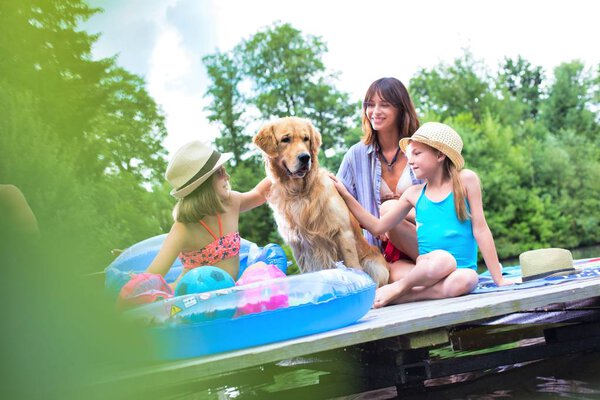 Золотистый ретривер сидит среди девушек и женщин на пирсе у деревьев
