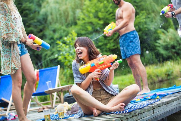 cheerful couples enjoying with water guns on pier during summer