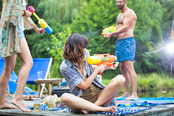 cheerful couples enjoying with water guns on pier during summer