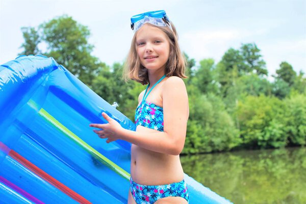smiling girl in swimwear standing with pool raft at lakeshore