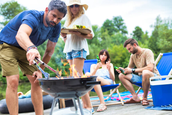Man using bellows for preparing food in barbecue grill with friends on pier