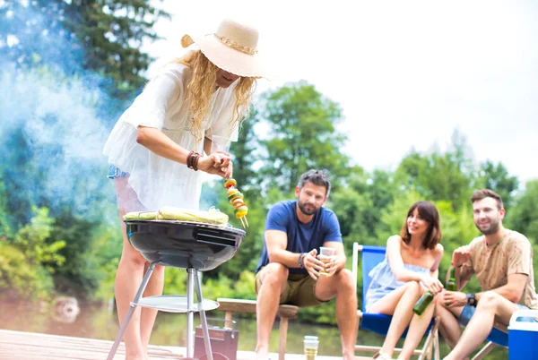 Woman preparing food in barbecue grill with friends on pier