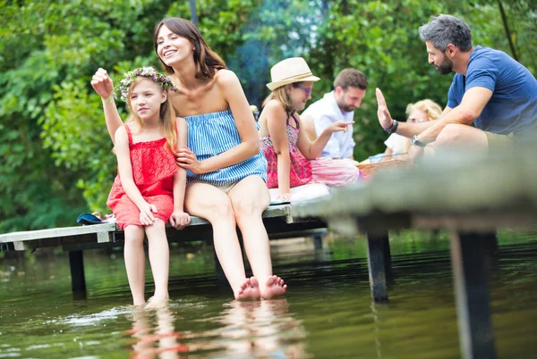 Mujer Sonriente Señalando Hija Mientras Sienta Muelle Contra Familia Orilla — Foto de Stock