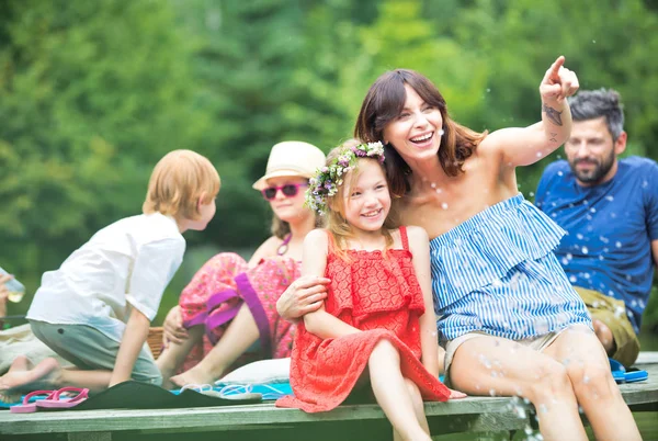 Mujer Sonriente Señalando Hija Mientras Sienta Muelle Contra Familia Orilla — Foto de Stock