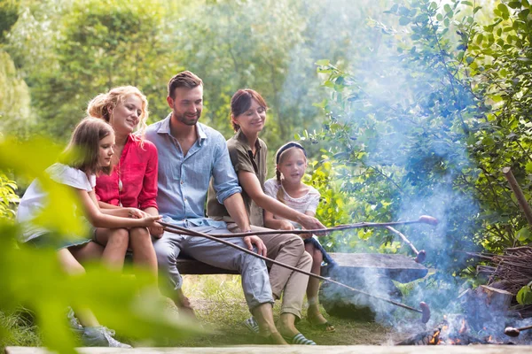 Happy family roasting sausages over campfire at park