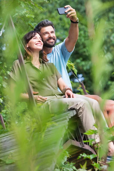 Pełna Długość Uśmiechnięta Kobieta Biorąc Selfie Człowiekiem Siedząc Deptaku Parku — Zdjęcie stockowe