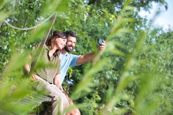 Pełna Długość Uśmiechnięta Kobieta Biorąc Selfie Człowiekiem Siedząc Deptaku Parku — Zdjęcie stockowe