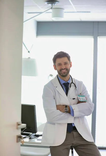 Porträtt av leende säker läkare med hjälp av dator vid skrivbordet i h — Stockfoto