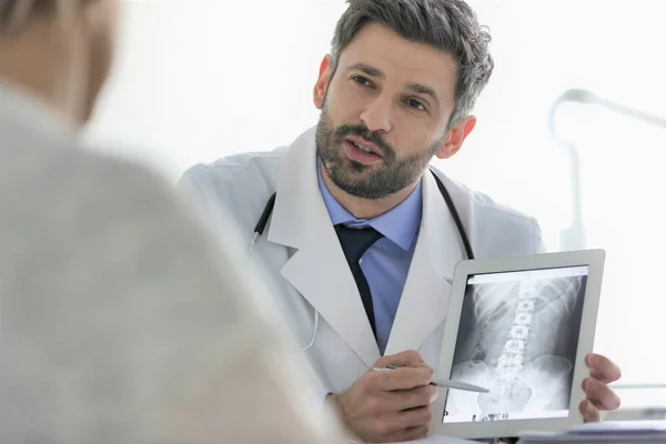 Врач объясняет рентген на цифровом планшете пациенту за письменным столом в — стоковое фото