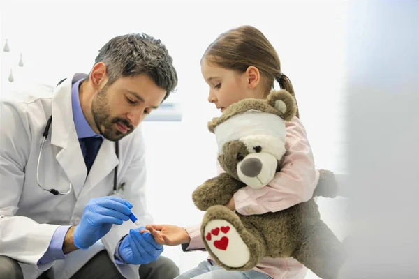 Yetişkin bir doktor hastanedeki oyuncak ayıyla kızı muayene ediyor. — Stok fotoğraf