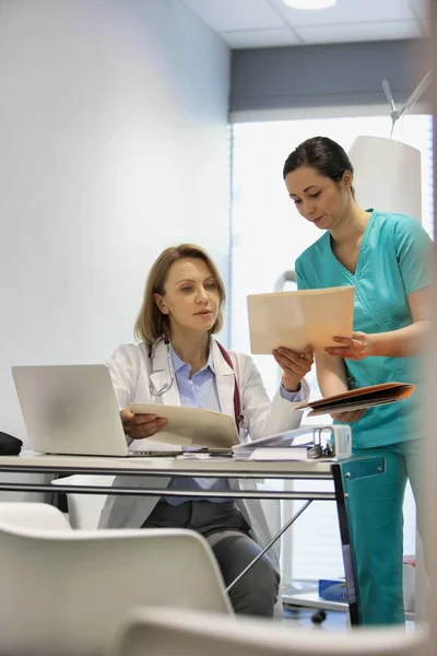 Enfermera mostrando expediente médico a médico maduro en el escritorio en el hospital —  Fotos de Stock