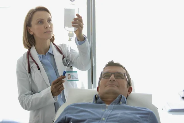 Mature doctor adjusting saline IV drip for patient in hospital w — Stock Photo, Image