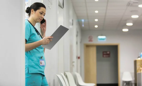Verpleegster praten op smartphone tijdens het lezen van document op klembord — Stockfoto