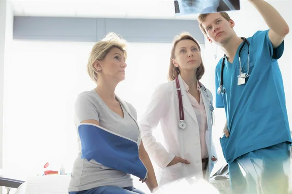 Fysiotherapeut discussieert over röntgenfoto aan verpleegkundige en patiënt op ho — Stockfoto