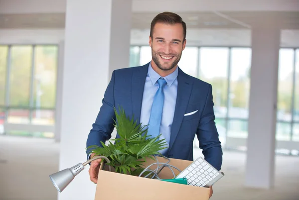 Smiling handsome young businessman standing with cardboard box i — Stock Photo, Image