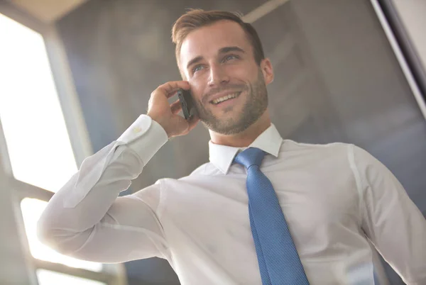 Buen hombre de negocios joven sonriendo mientras habla por teléfono inteligente —  Fotos de Stock