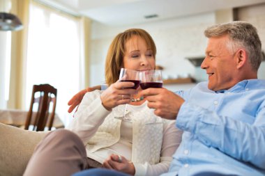 Evde içki içerken koltukta oturan gülümseyen olgun bir çift.