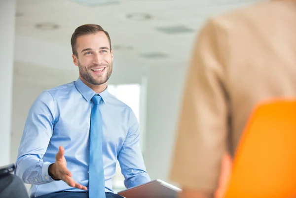 Glimlachende jonge zakenman zit met collega tijdens vergadering — Stockfoto