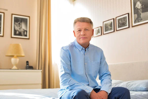 Portrait of mature man sitting on bed at home — Stock Photo, Image