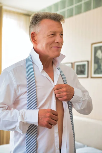 Sorrindo homem de negócios abotoando camisa enquanto olha para longe no leito — Fotografia de Stock