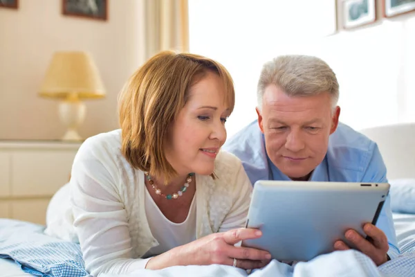 Leende Mogna Par Dela Digital Tablett När Ligger Sängen Hemma — Stockfoto